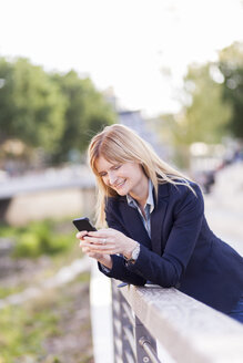 Smiling businesswoman leaning on railing looking at cell phone - NAF000029