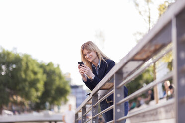 Geschäftsfrau lehnt am Geländer und schaut auf ihr Handy - NAF000030