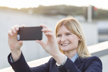 Porträt einer lächelnden blonden Geschäftsfrau, die ein Selfie mit ihrem Smartphone macht - NAF000042
