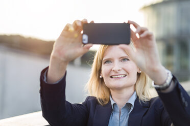 Porträt einer lächelnden blonden Geschäftsfrau, die ein Selfie mit ihrem Smartphone macht - NAF000043