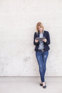 Smiling businesswoman leaning against wall looking at tablet - NAF000045