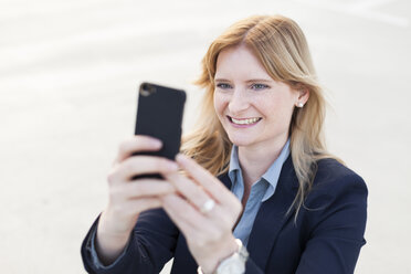 Porträt einer lächelnden blonden Geschäftsfrau, die ein Selfie mit ihrem Smartphone macht - NAF000054