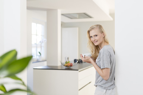 Lächelnde blonde Frau mit einer Tasse Kaffee in der Küche, lizenzfreies Stockfoto