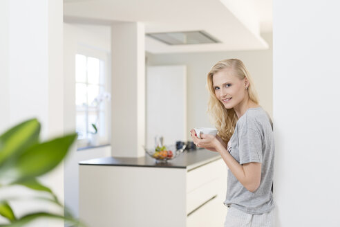 Lächelnde blonde Frau mit einer Tasse Kaffee in der Küche - SHKF000647