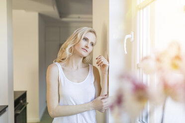 Blonde Frau zu Hause, die aus dem Fenster schaut - SHKF000650