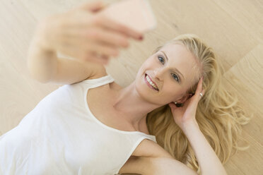 Blonde Frau liegt auf Holzboden und macht ein Selfie - SHKF000654
