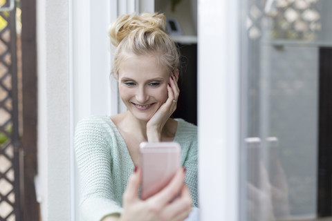 Blond woman sitting at terrace door holding cell phone stock photo