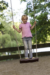 Little girl standing on a swing at playground - JFEF000803