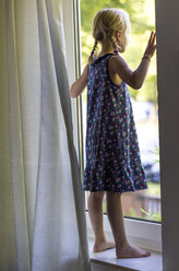 Little girl standing on window sill looking through window - JFEF000805