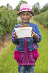 Porträt eines glücklichen kleinen Mädchens mit einer Kiste Erdbeeren auf einem Erdbeerfeld - JFEF000812