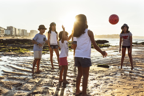 Kinder spielen mit einem Ball am Strand bei Sonnenuntergang, lizenzfreies Stockfoto