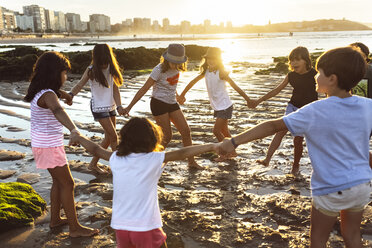 Hand in Hand spielende Kinder am Strand bei Sonnenuntergang - MGOF002298