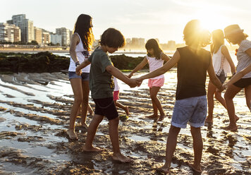 Kids playing hand in hand on the beach at sunset - MGOF002299