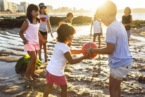 Kids playing with a ball on the beach at sunset stock photo