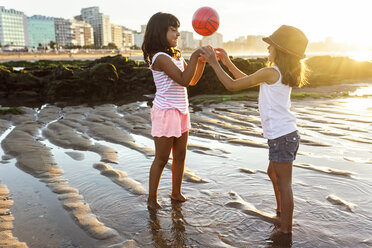 Zwei Mädchen spielen mit einem Ball am Strand bei Sonnenuntergang - MGOF002305
