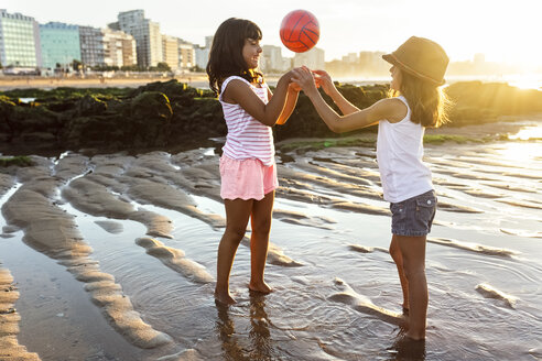 Zwei Mädchen spielen mit einem Ball am Strand bei Sonnenuntergang - MGOF002305