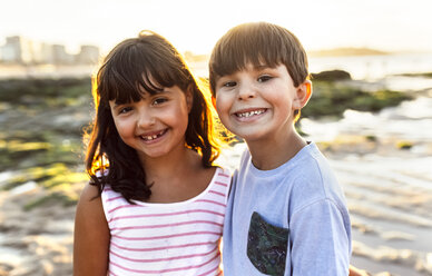 Porträt von zwei lächelnden Kindern am Strand bei Sonnenuntergang - MGOF002308