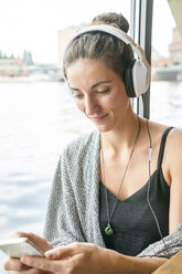 Lächelnde junge Frau, die mit Kopfhörern Musik hört und auf ihr Mobiltelefon schaut - TAMF000566