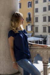 Happy blond woman leaning against column - MAUF000840