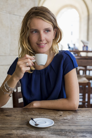 Porträt einer lächelnden blonden Frau, die in einem Straßencafé Espresso trinkt, lizenzfreies Stockfoto