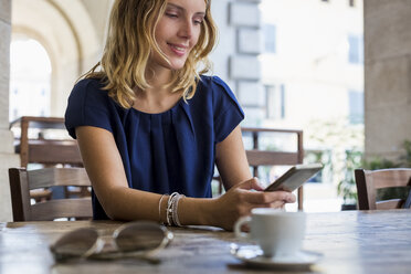 Smiling woman sitting in a sidewalk cafe, looking at cell phone - MAUF000847