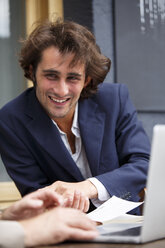 Smiling young businessman talking at sidewalk cafe - TAMF000584