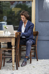 Lächelnder junger Geschäftsmann arbeitet mit Laptop in einem Straßencafé - TAMF000586