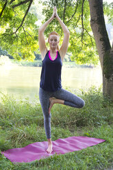 Young woman doing yoga on gym mat on a meadow - YFF000563