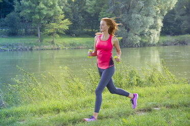 Junge Frau joggt mit Hanteln am Flussufer - YFF000566