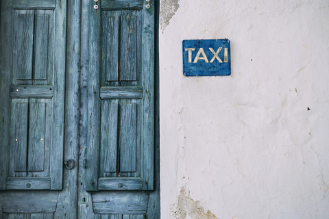 Griechenland, Kykladen, blaue Holztür und Taxischild an der Fassade, lizenzfreies Stockfoto