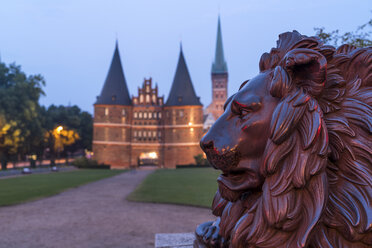 Germany, Luebeck, lion statue in front of the town gate Holstentor and Church of St. Peter at dusk - PCF000262