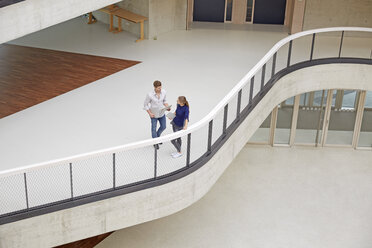 Young man and woman talking in modern office building - FMKF003053