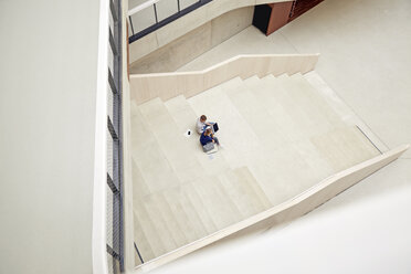 Young man and woman sitting on staircase in a building using laptop - FMKF003054