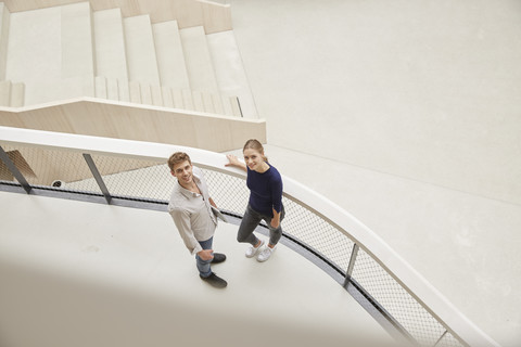 Junger Mann und Frau in Bürogebäude mit Blick nach oben, lizenzfreies Stockfoto