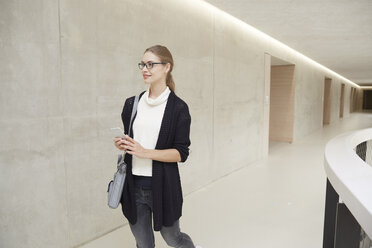 Lächelnde junge Frau auf dem Korridor eines Gebäudes - FMKF003064