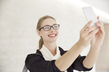 Smiling young woman with glasses taking a selfie - FMKF003065