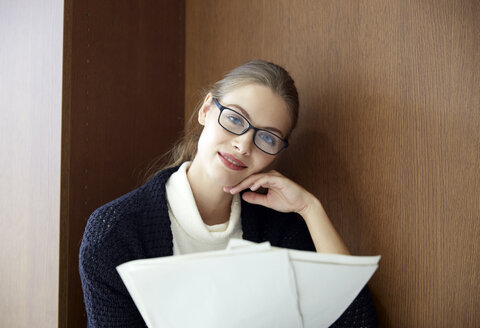 Porträt einer jungen Frau mit Brille, die Dokumente hält - FMKF003069