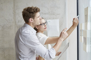 Young man and woman working on draft on glass pane - FMKF003074