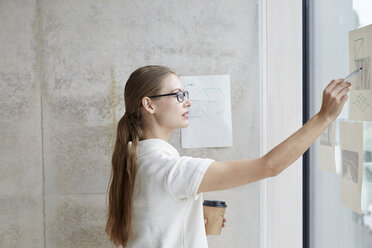 Young woman looking at draft on glass pane - FMKF003076