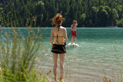 Österreich, Tirol Ammergauer Alpen, Plansee, Jugendlicher auf Paddelbrett stehend, Schwester wartet am Seeufer - LBF001456