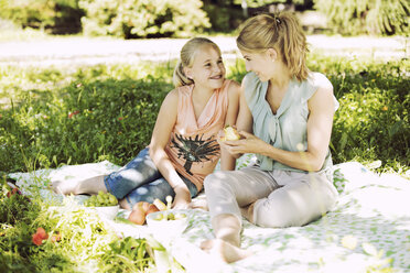 Smiling girl and young woman sitting face to face on blanket in a park - GDF001110