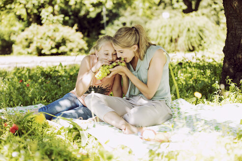 Mädchen und junge Frau sitzen zusammen auf einer Decke in einem Park und essen Weintrauben - GDF001112