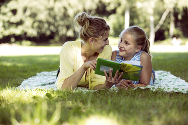 Girl and young woman with book lying on blanket in a park - GDF001115