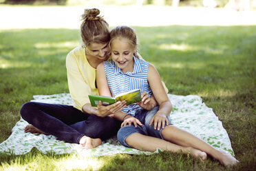 Mädchen und junge Frau sitzen auf einer Decke in einem Park und lesen ein Buch - GDF001117