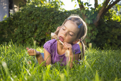 Little girl lying on meadow eating ice lolly - LVF005211