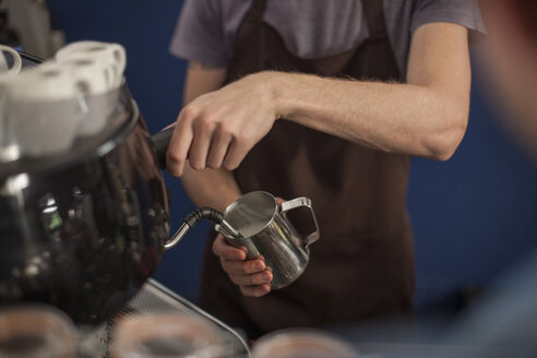 Junger Barista schäumt Milch aus einer Kanne auf - ZEF009843