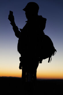 Silhouette eines Wanderers, der auf sein Smartphone schaut - MIDF000787