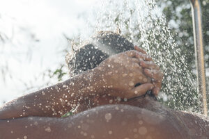 Back view of young man taking shower in garden - SKCF000180
