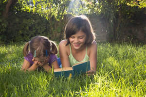 Mädchen auf einer Wiese liest ihrer kleinen Schwester ein Buch vor - LVF005227