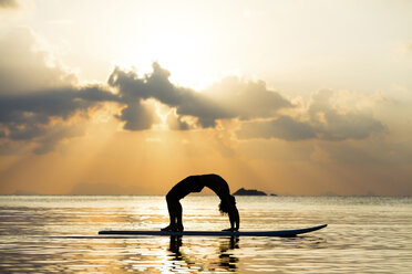 Thailand, Mann macht Yoga auf Paddleboard bei Sonnenuntergang, Brückenposition - SBOF000177